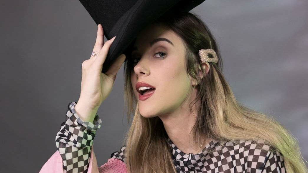 A smiling woman lifting a top hat from her head