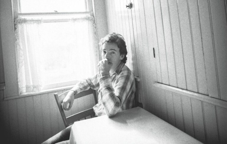 Bruce Springsteen in black-and-white sat at a kitchen table by a window