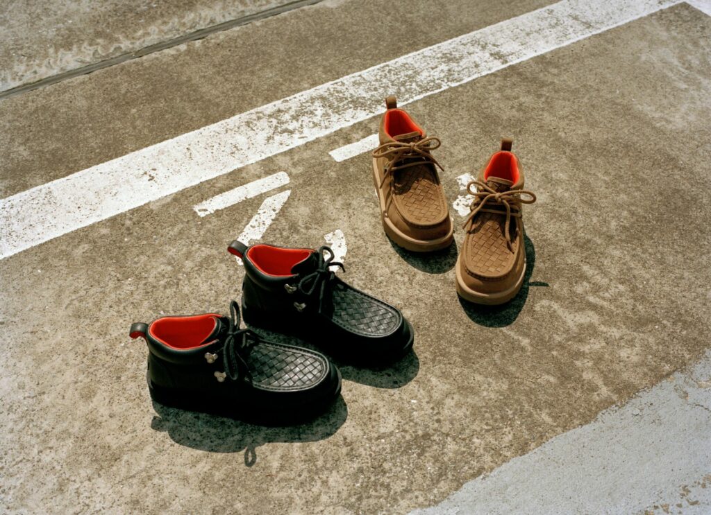 A product shot of the new AMBUSH and UGG Autumn/Winter 2025 Woven boots in black and brown. 