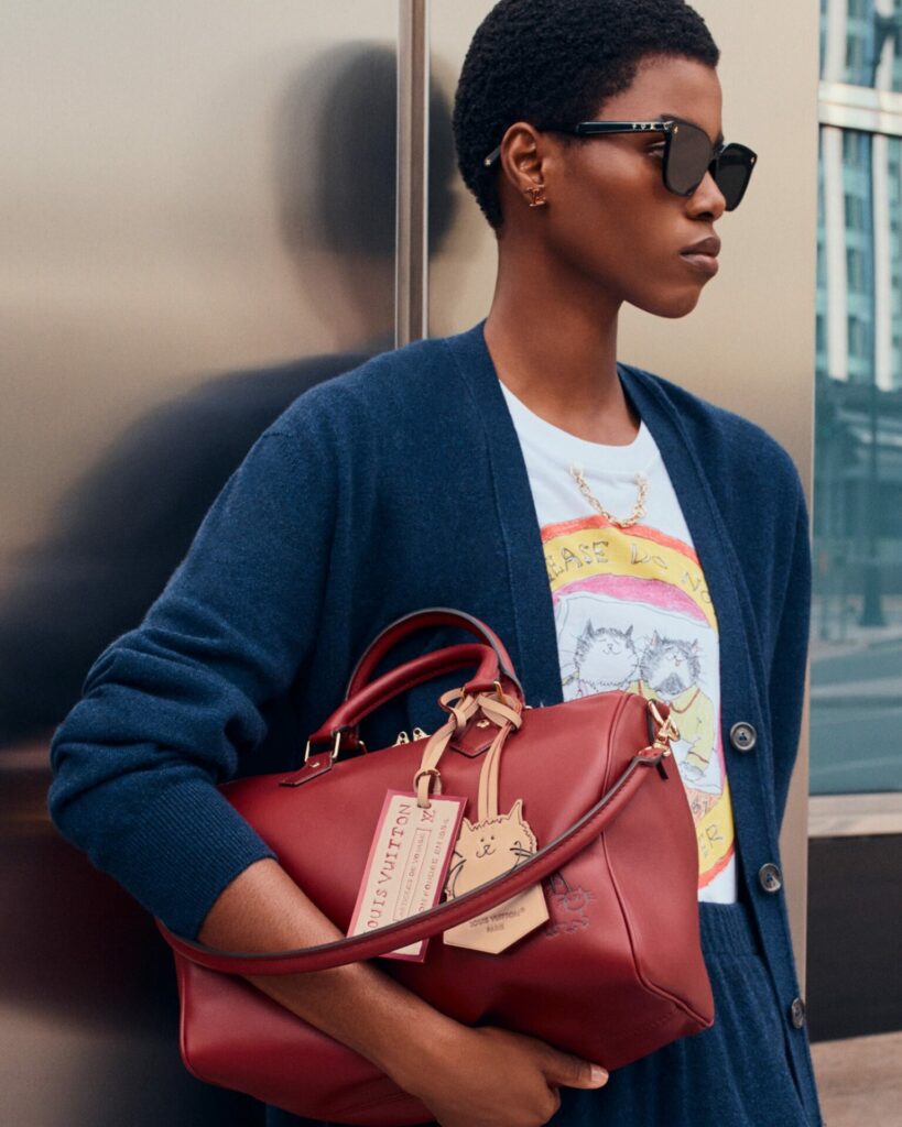A lifestyle shot of a model carrying a red bag from the Louis Vuitton Travels with Grace Coddinton collection