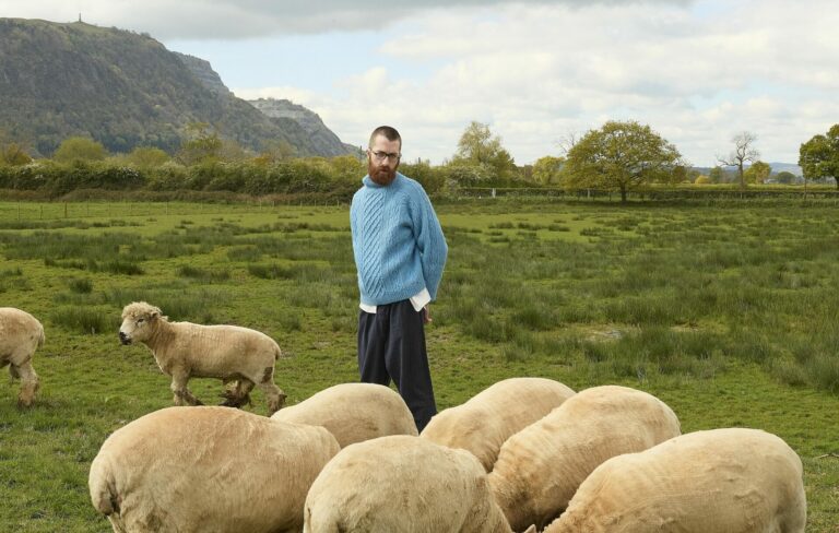 Jerskin Fendrix poses for a photoshoot in a field surrounded by sheep