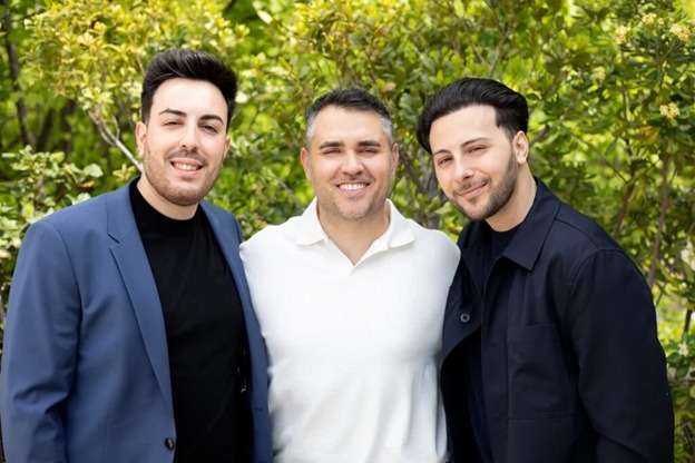 Three smiling men standing in front of green trees