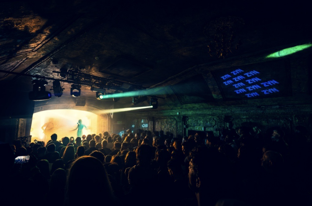 A performer on stage singing at Omera London with ZYN branding on the wall
