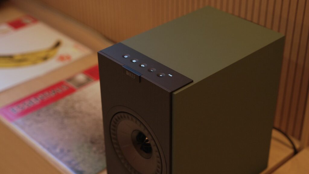 A KEF Coda W speaker in Moss Green, photographed at the KEF & Flashback Records: The Resurgence of Vinyl event, with a vinyl record sleeve visible in the background.