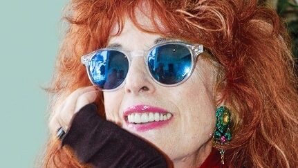 Close crop of Carolyn Campagna Kleefeld smiling with red hair and blue sunglasses